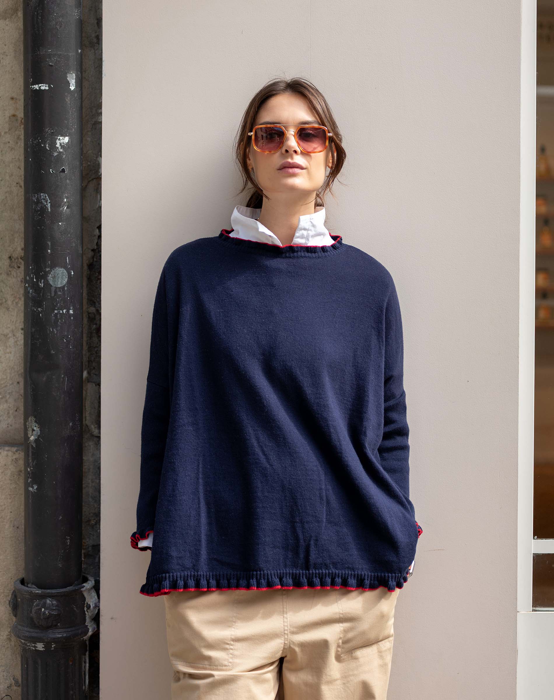 Woman wearing a navy sweater with red trim against a neutral wall.
