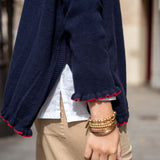 Navy blue sweater with red trim worn by a person, with a blurred background.