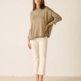 Woman wearing a green sweater and white pants against a plain background