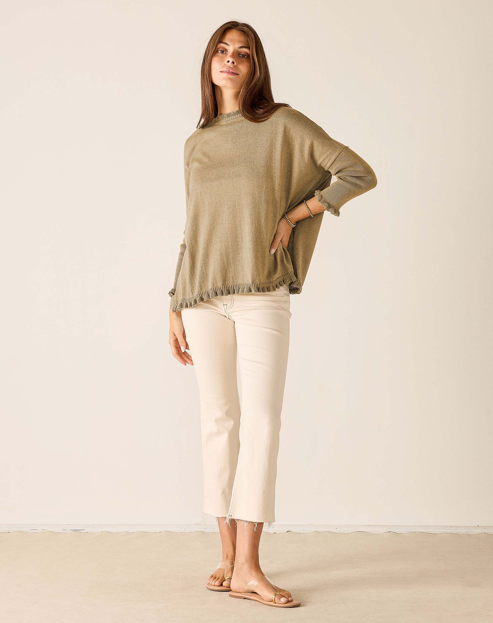 Woman wearing a green sweater and white pants against a plain background