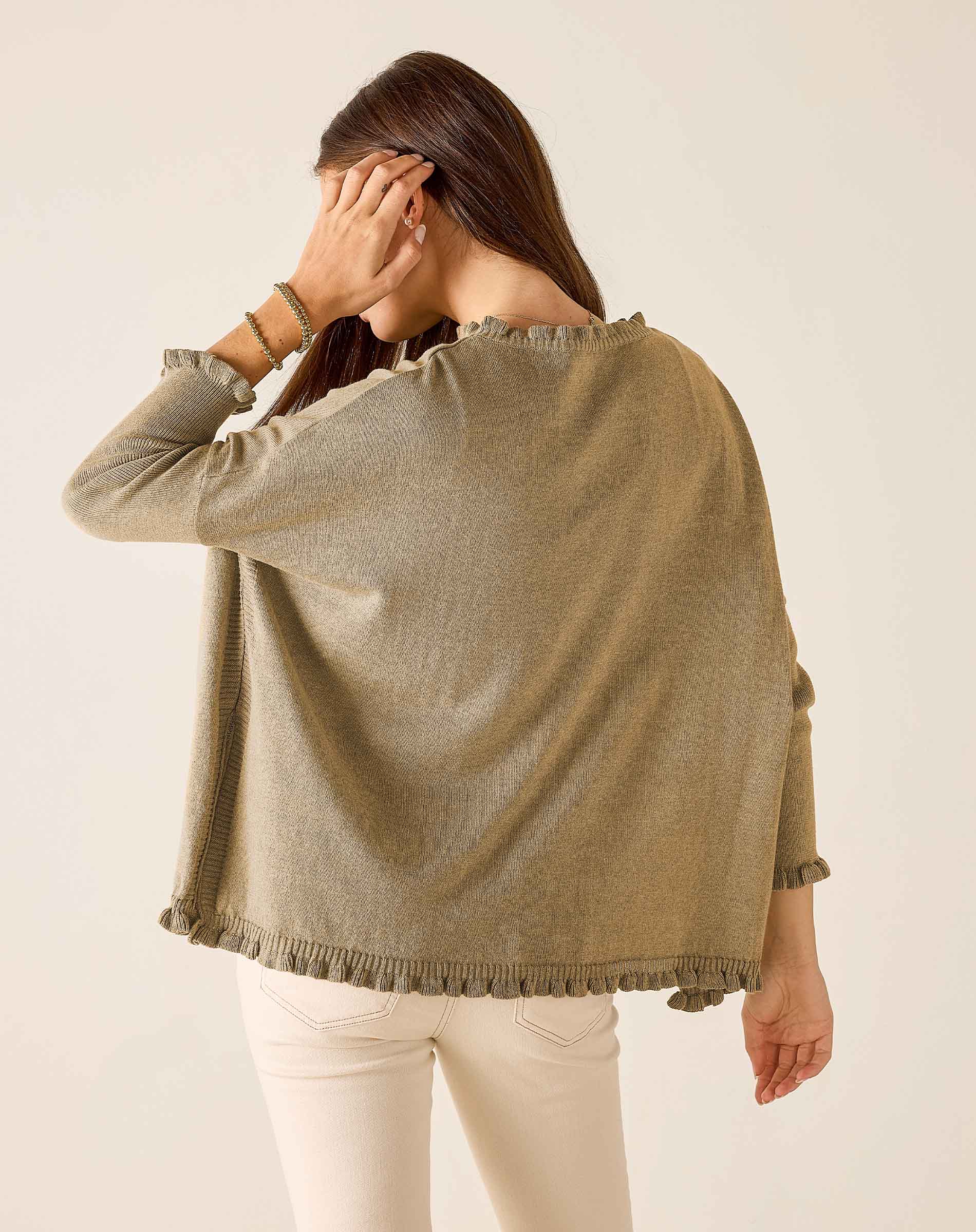 Woman wearing a beige knitted poncho against a plain background