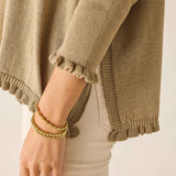 Close-up of a person wearing a beige sweater with ruffled cuffs and a bracelet on a neutral background