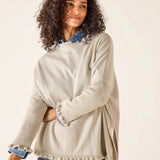 Woman wearing a beige sweater over a denim shirt on a plain background