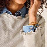 Person wearing a beige sweater with a blue shirt peeking out of the pocket.