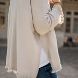 Person wearing a beige cardigan over a white shirt with a blurred background