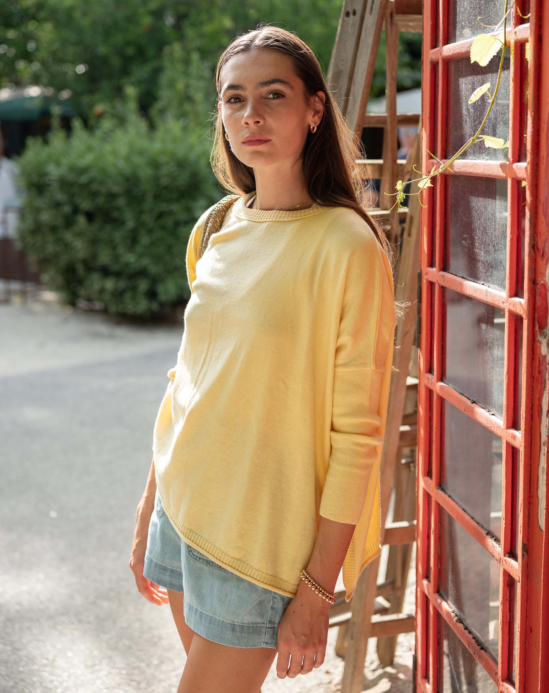 Woman in a yellow shirt standing outdoors near a red metal structure.