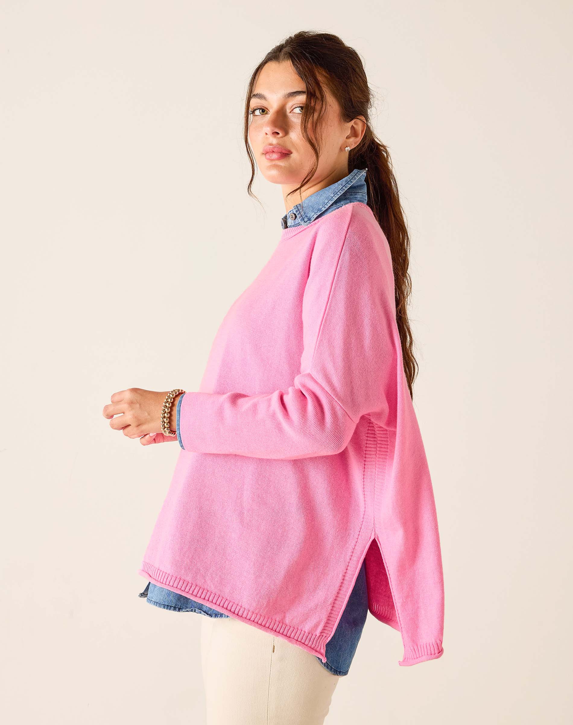 Woman wearing a pink sweater over a denim shirt on a beige background