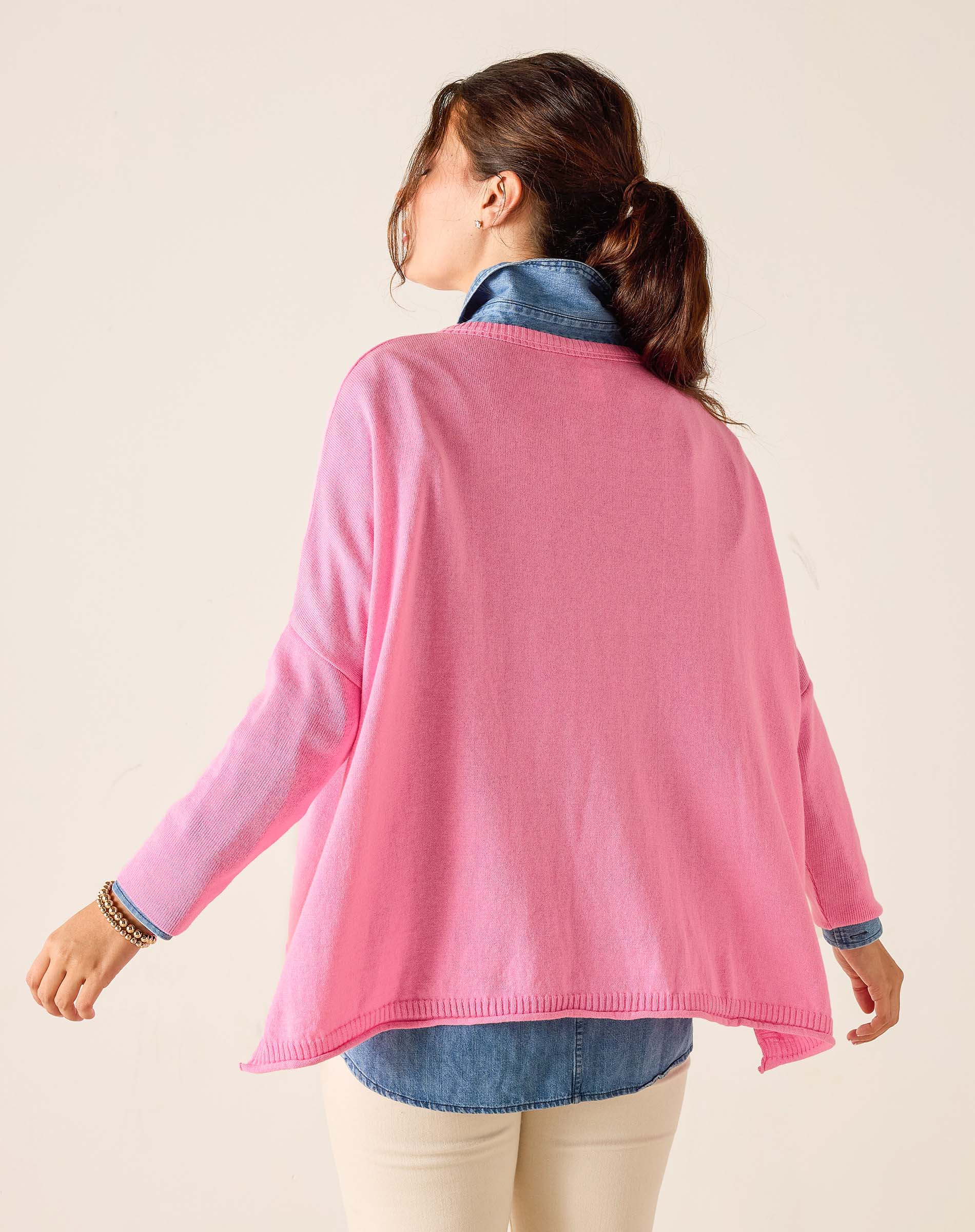Woman wearing a pink cardigan over a denim shirt on a beige background