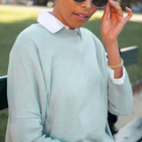 Person wearing a light green sweater with a white collar, sitting outdoors.