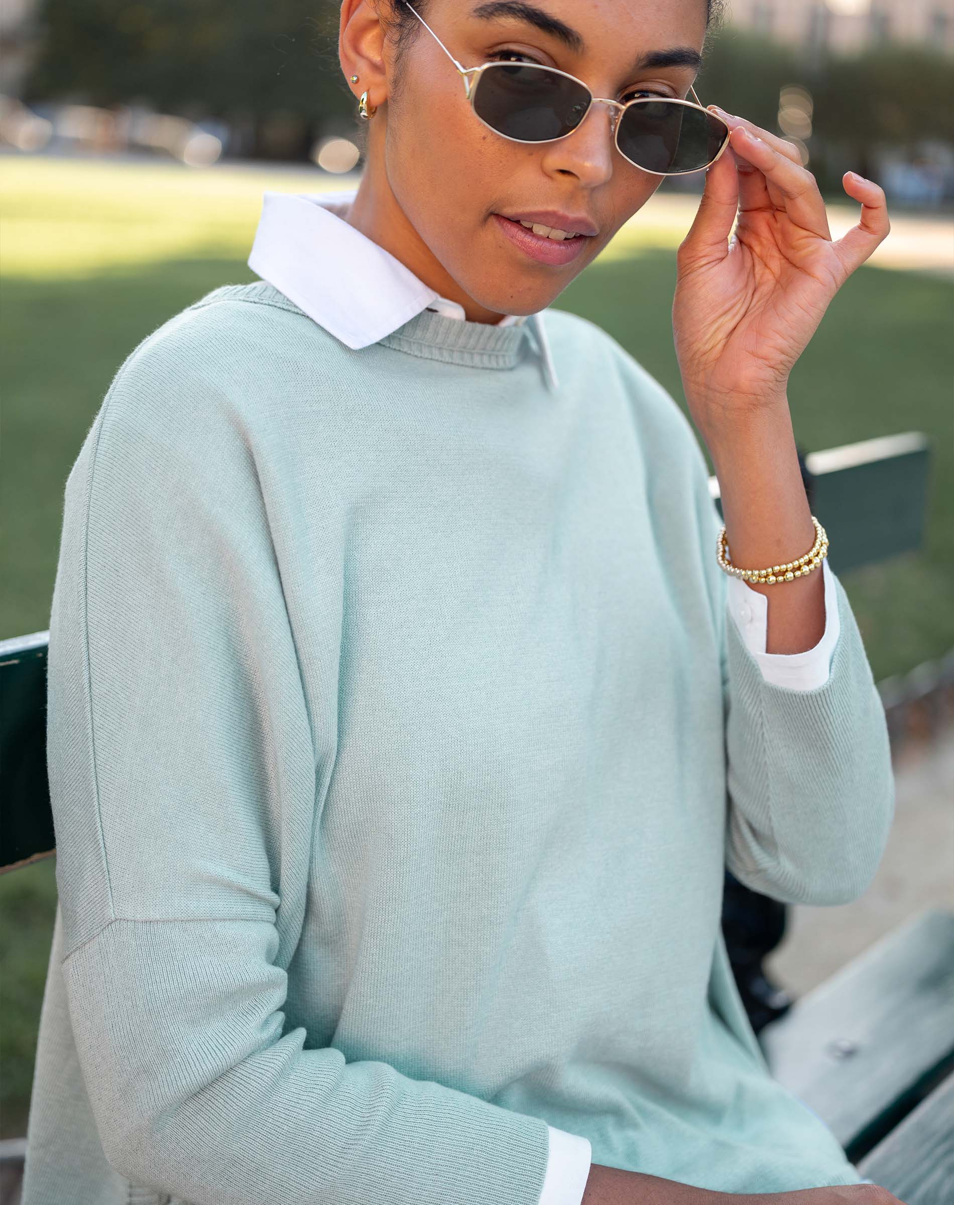 Person wearing a light green sweater with a white collar, sitting outdoors.