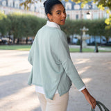 Woman in a light green jacket and white shirt walking outdoors.