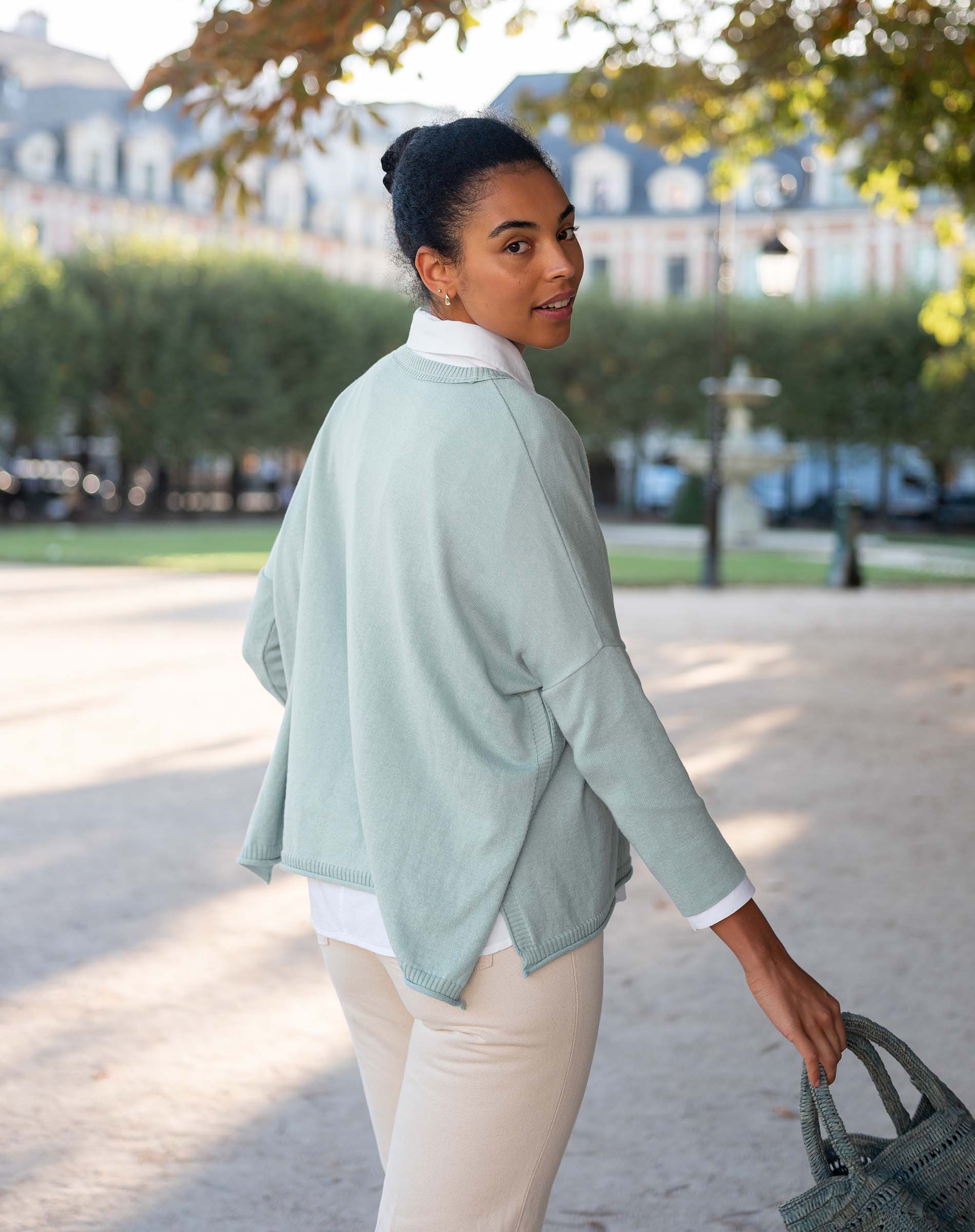 Woman in a light green jacket and white shirt walking outdoors.