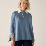 Woman wearing a blue sweater with white collar and cuffs on a plain background