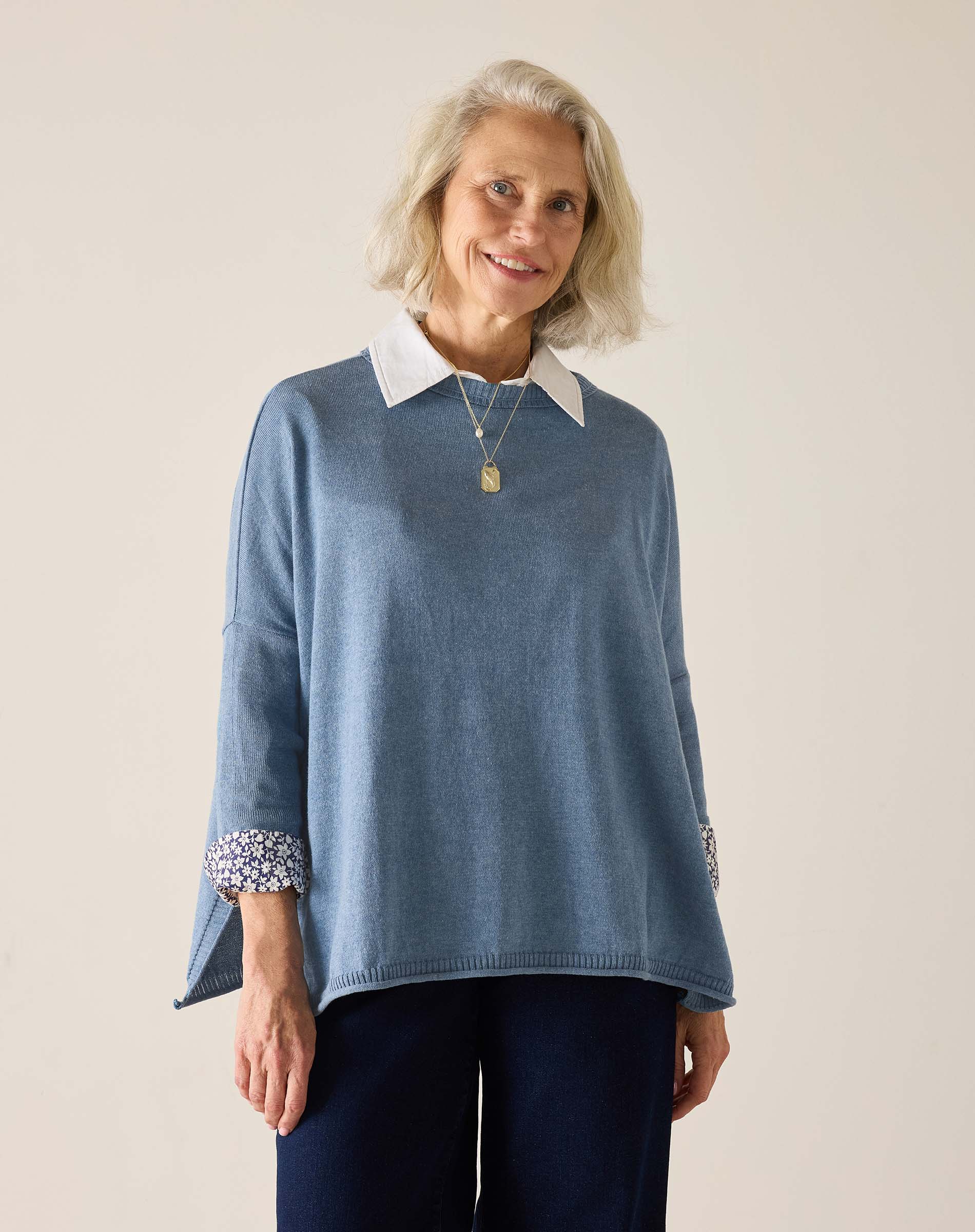 Woman wearing a blue sweater with white collar and cuffs on a plain background