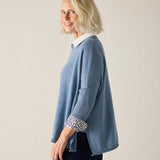 Woman wearing a blue sweater with rolled-up sleeves against a plain background