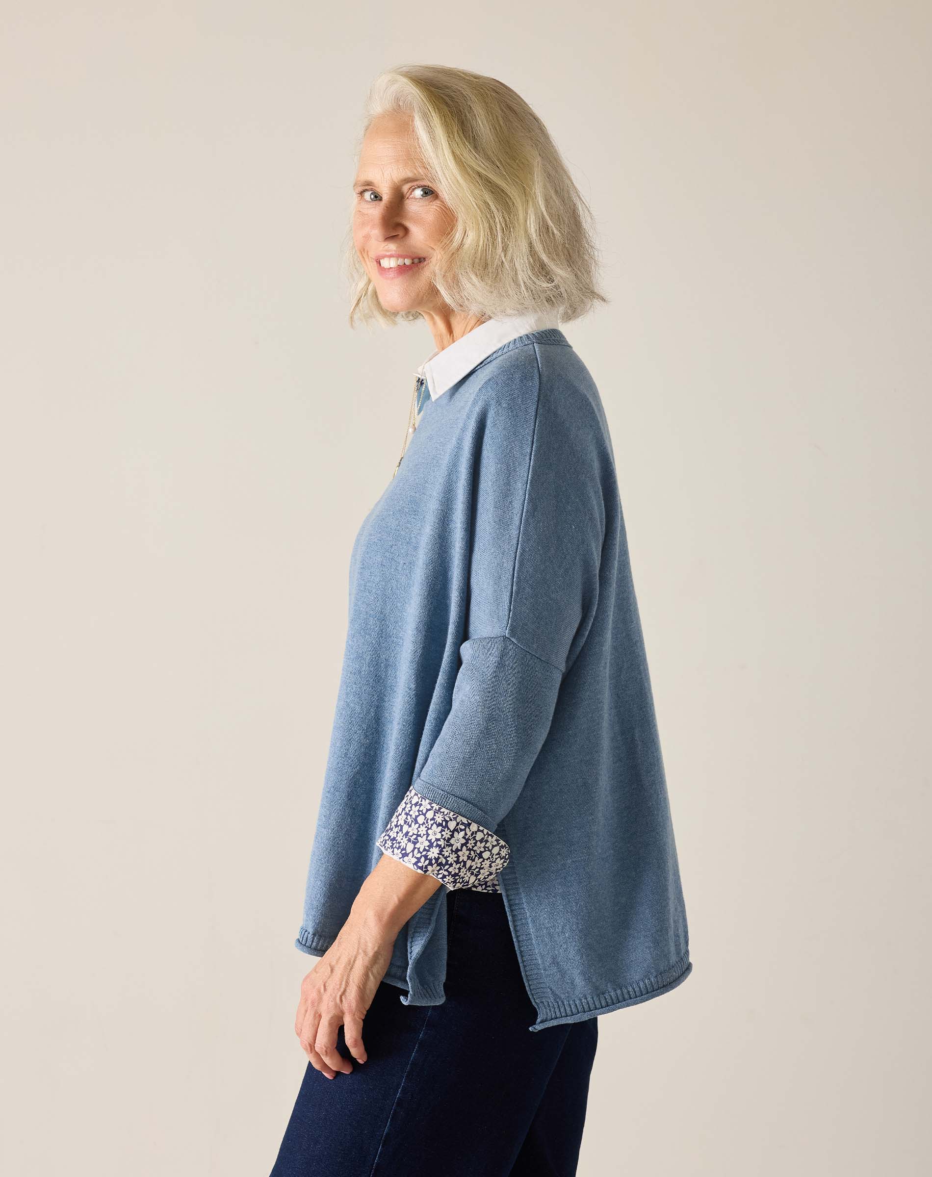Woman wearing a blue sweater with rolled-up sleeves against a plain background