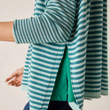 Side view of a teal and white striped knit crewneck sweater with an open side slit.