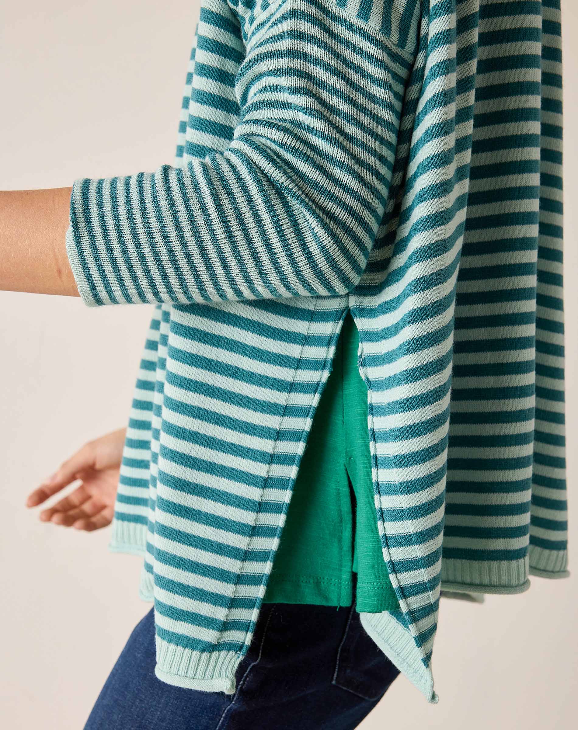Side view of a teal and white striped knit crewneck sweater with an open side slit.
