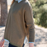 Tan and olive jungle stripe knit crewneck top worn over a light blue button-down shirt.