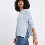Woman wearing a light blue poncho and jeans on a white background