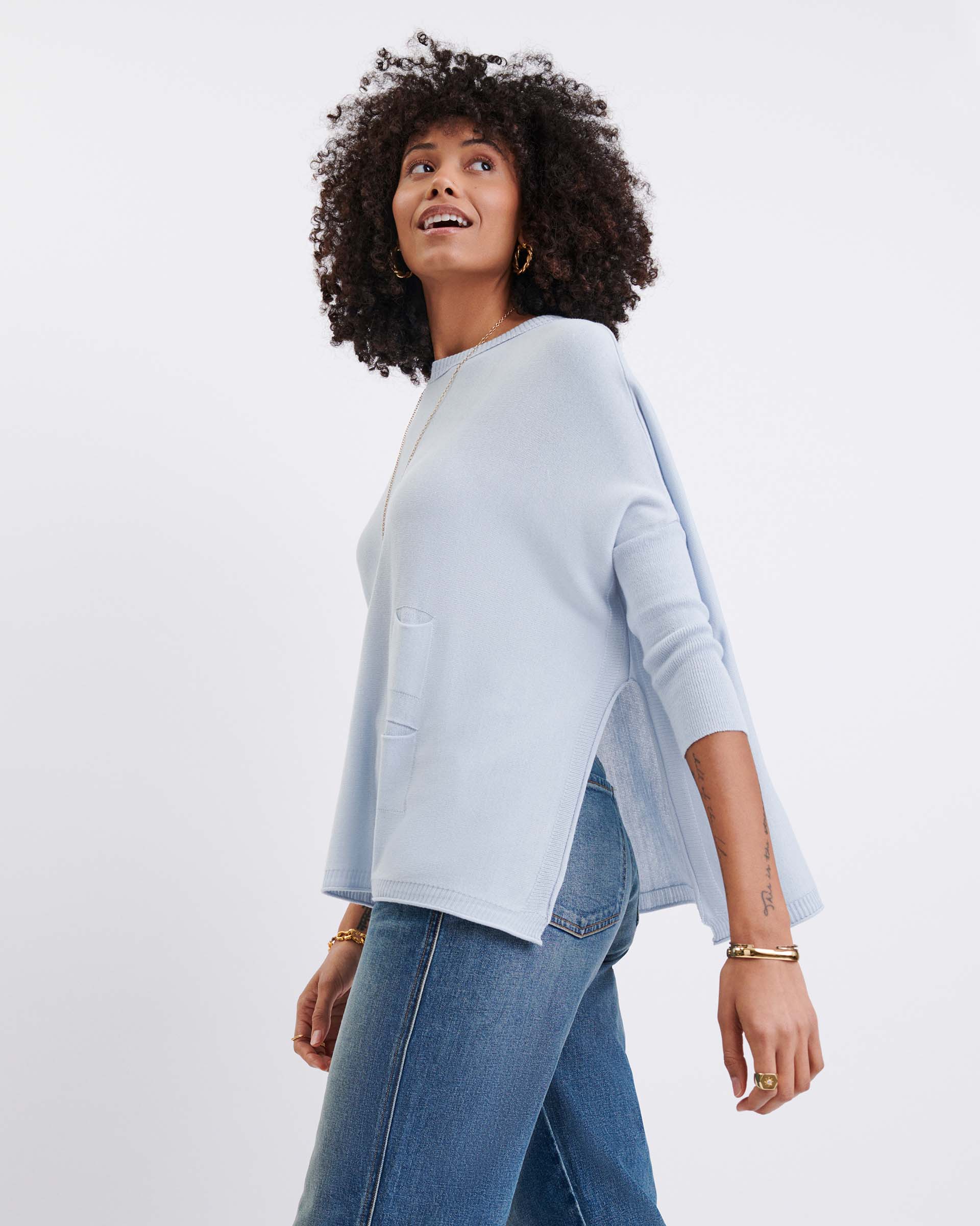 Woman wearing a light blue poncho and jeans on a white background
