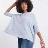 Woman wearing a light blue poncho and jeans on a white background