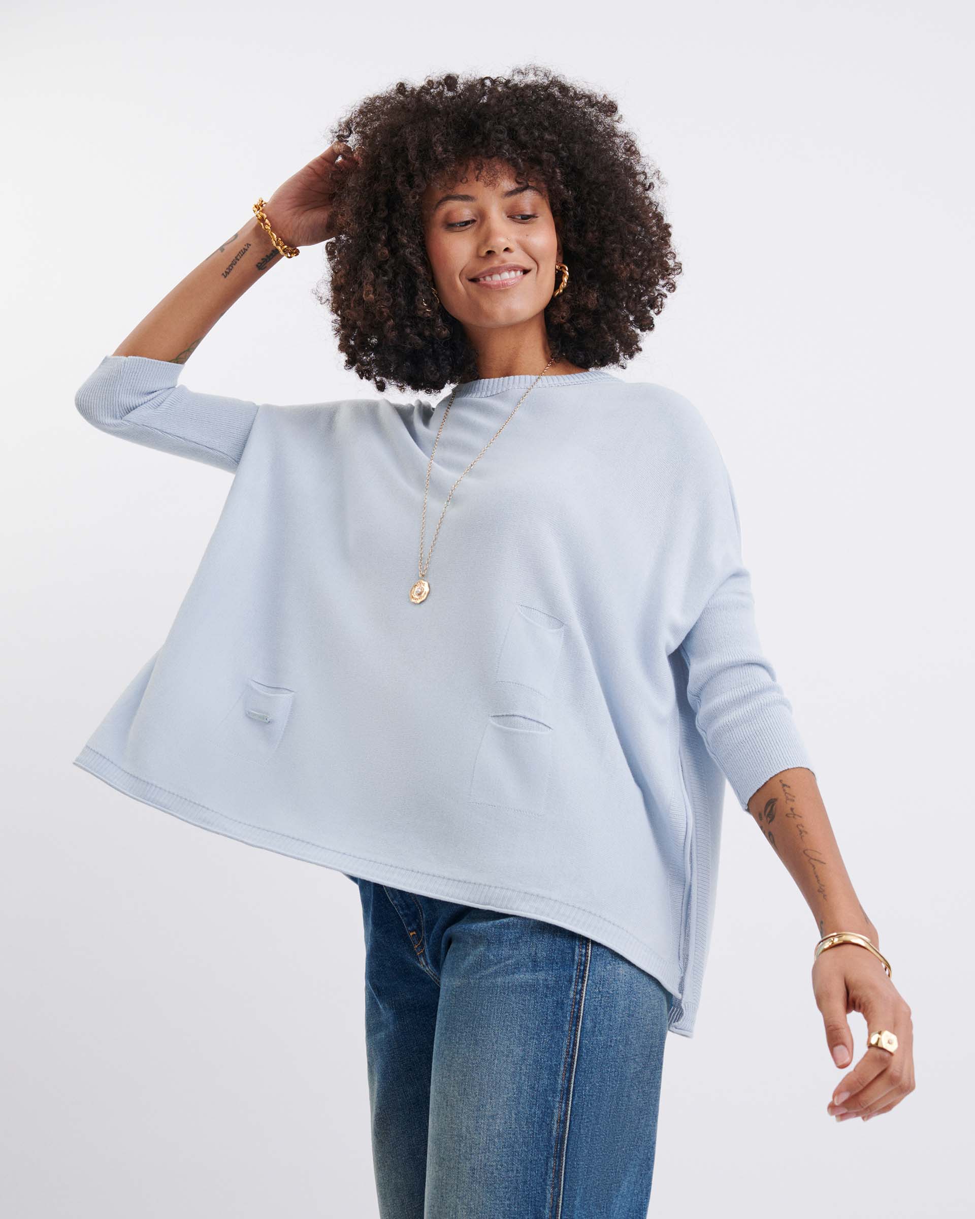 Woman wearing a light blue poncho and jeans on a white background