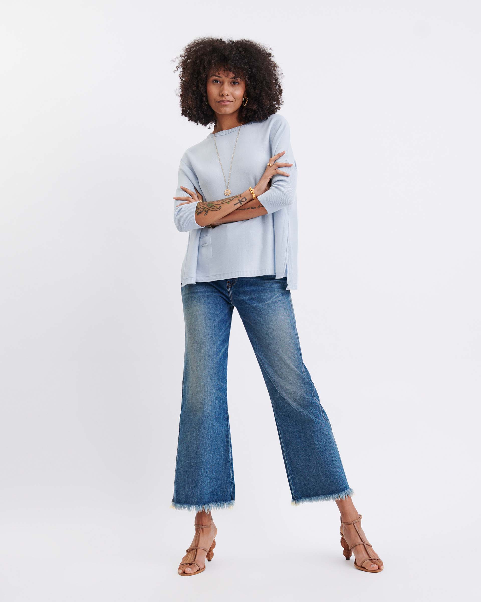 Woman wearing a light blue sweater and blue jeans on a white background