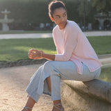 Woman sitting on a stone bench in a park wearing a pink cardigan and light blue pants.
