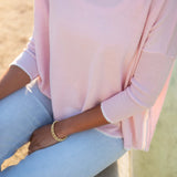 Person wearing a light pink sweater and light blue jeans with a blurred natural background