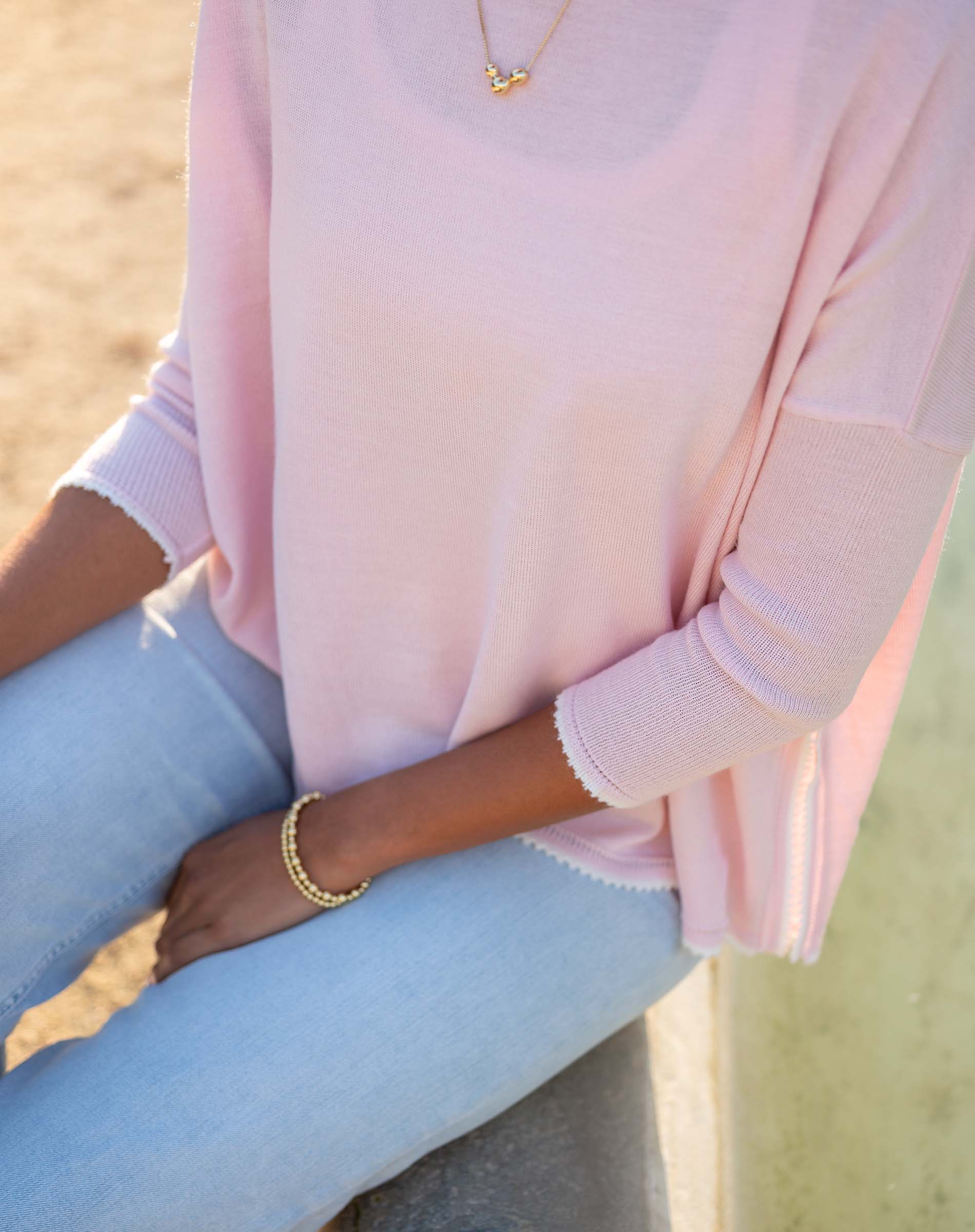 Person wearing a light pink sweater and light blue jeans with a blurred natural background