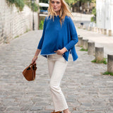 Woman in a blue sweater and white pants walking on a stone path.