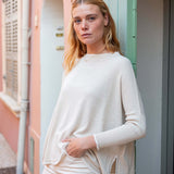 Woman in a white sweater standing in front of a pastel-colored building.