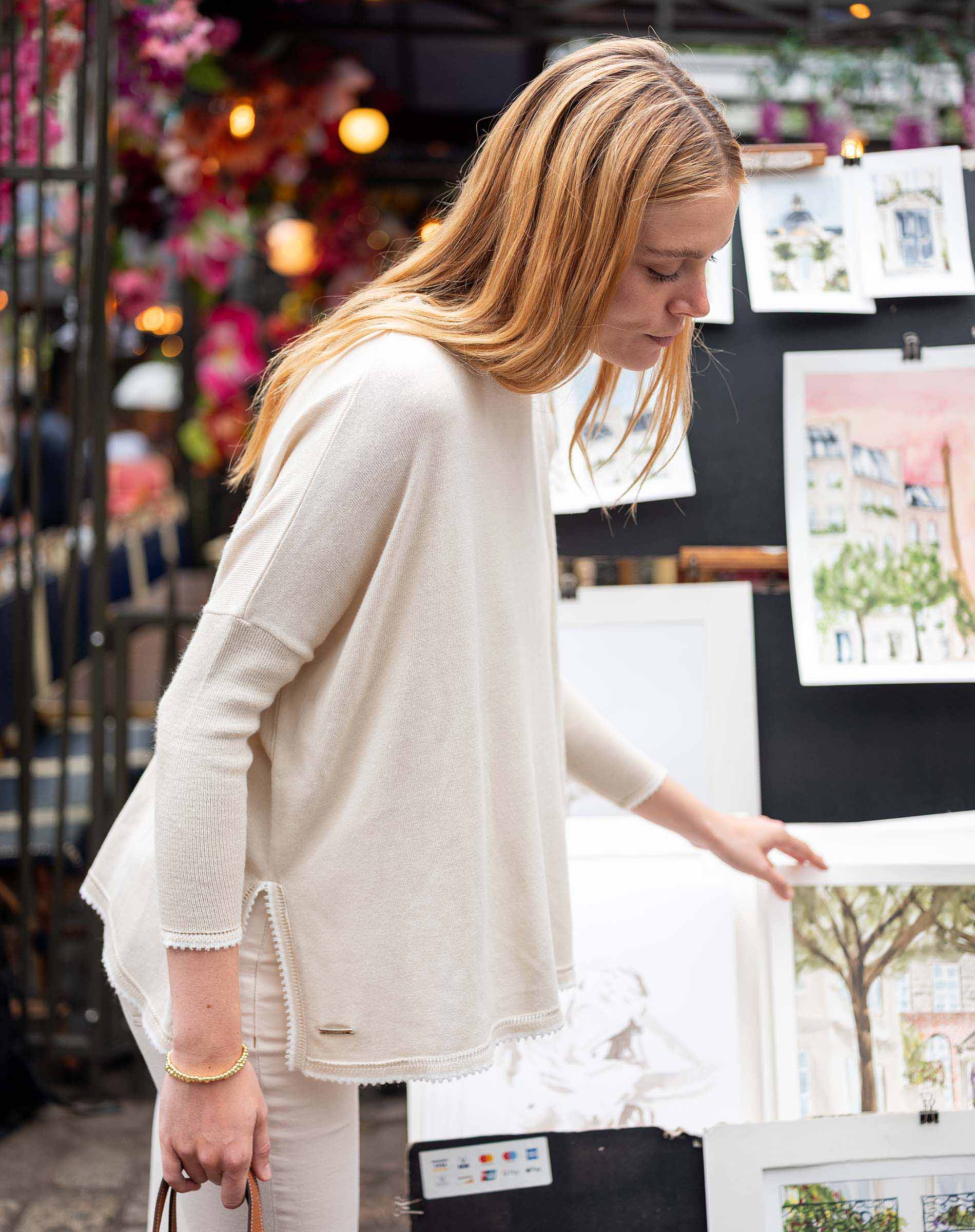 Woman in a white sweater looking at prints on a stand with a blurred background