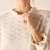 Ladies' travel-ready cream knit sweater with pointelle stitch pattern and ruffled neckline.