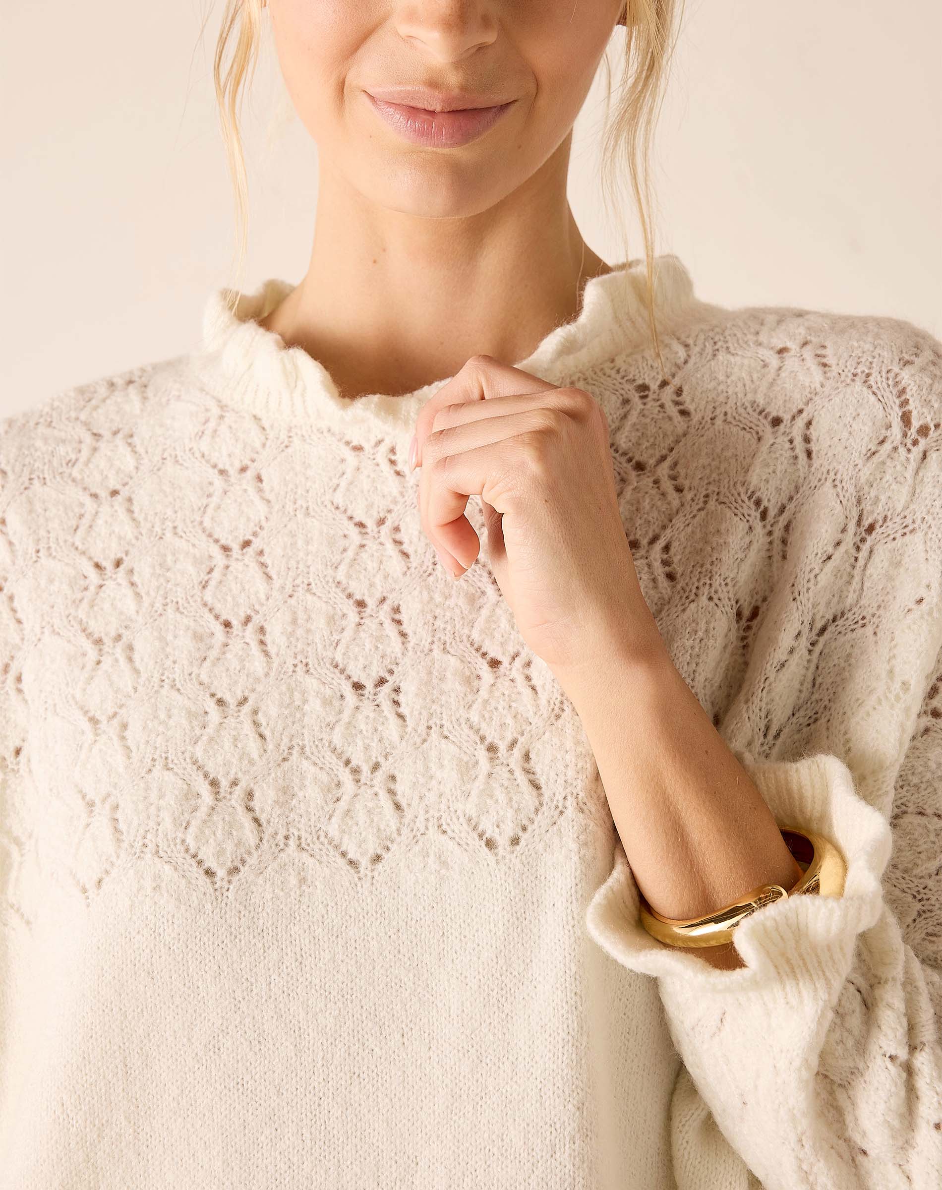 Ladies' travel-ready cream knit sweater with pointelle stitch pattern and ruffled neckline.