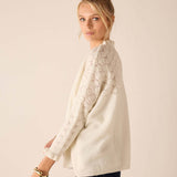 Cream cable-knit sweater with openwork details and decorative knit stitch patterns on sleeves.
