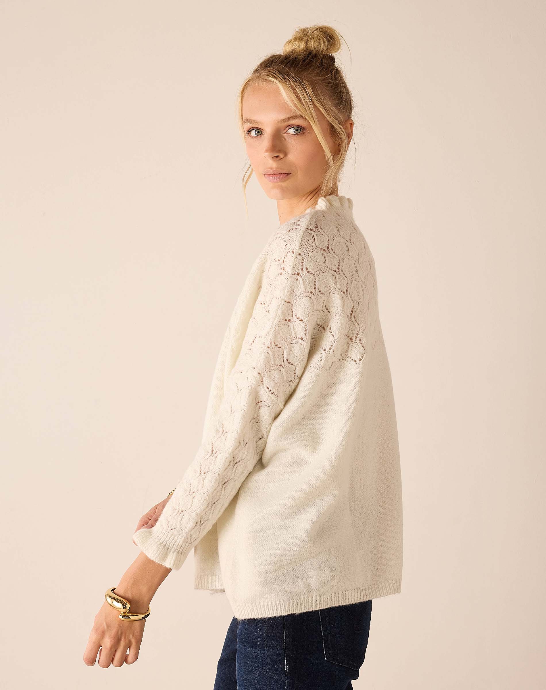 Cream cable-knit sweater with openwork details and decorative knit stitch patterns on sleeves.
