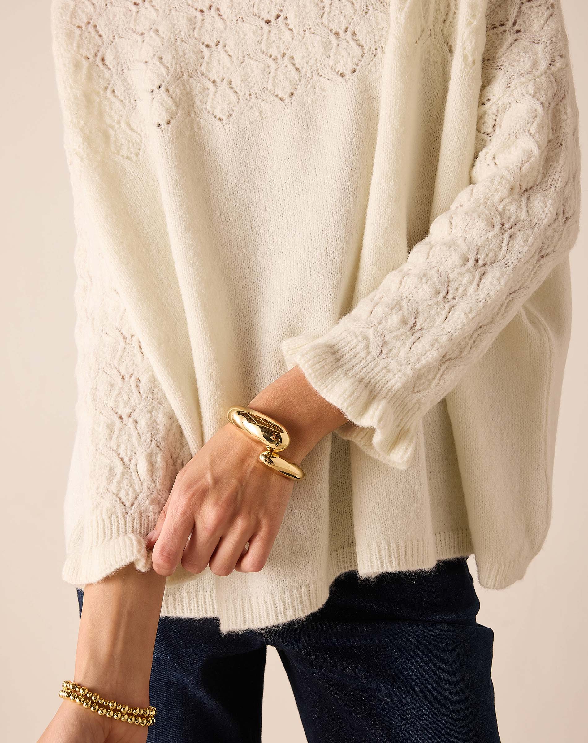 Cream-colored knit sweater featuring a pointelle stitch pattern and textured weave.