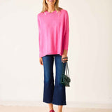 Woman wearing a bright pink top and blue jeans with a green bag on a white background