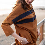 Woman wearing a brown dress with a blue stripe, standing outdoors.