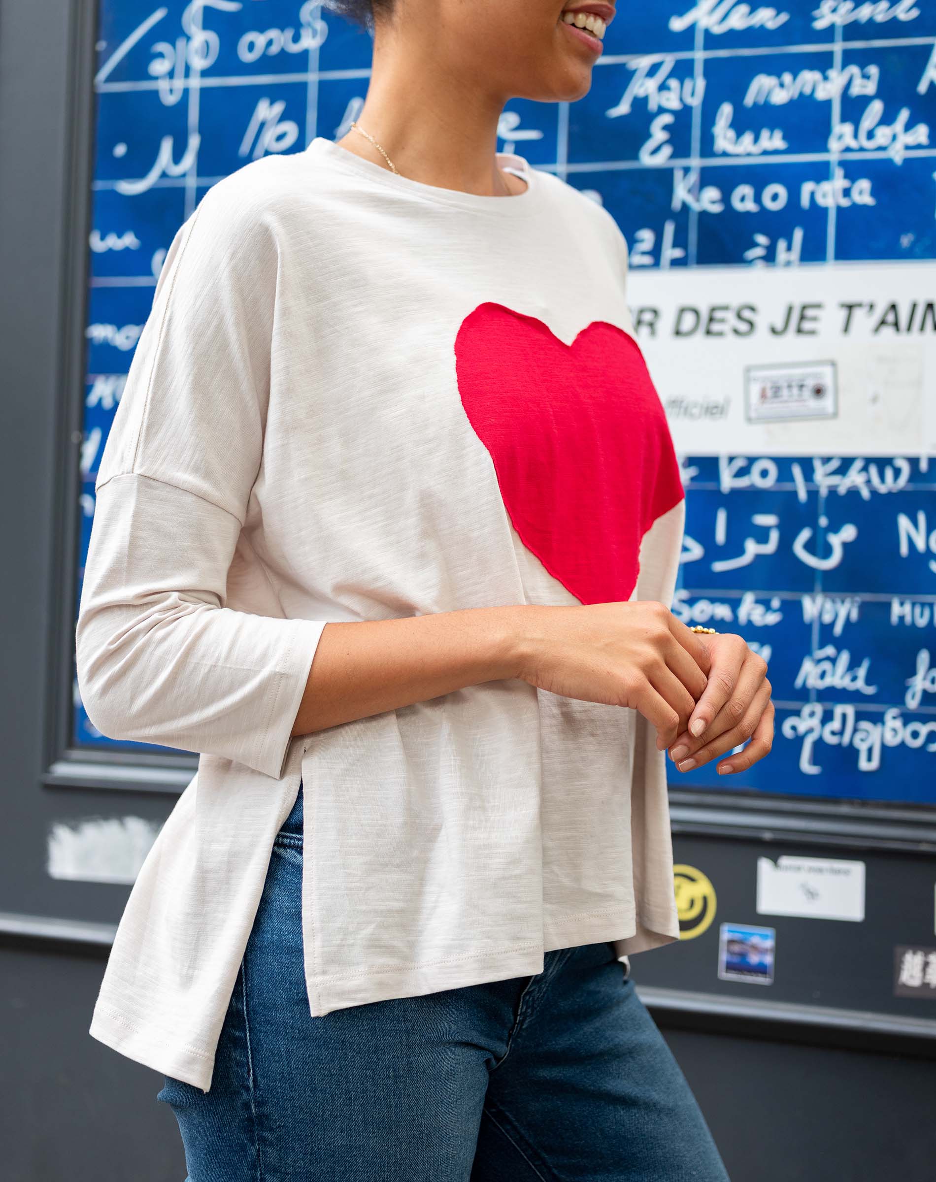 Person wearing a white long-sleeve shirt with a red heart design in front of a blue board with writing.