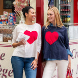 Two women wearing sweatshirts with red hearts standing in front of a store.