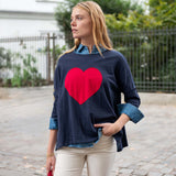 Woman wearing a navy sweater with a red heart design outdoors.