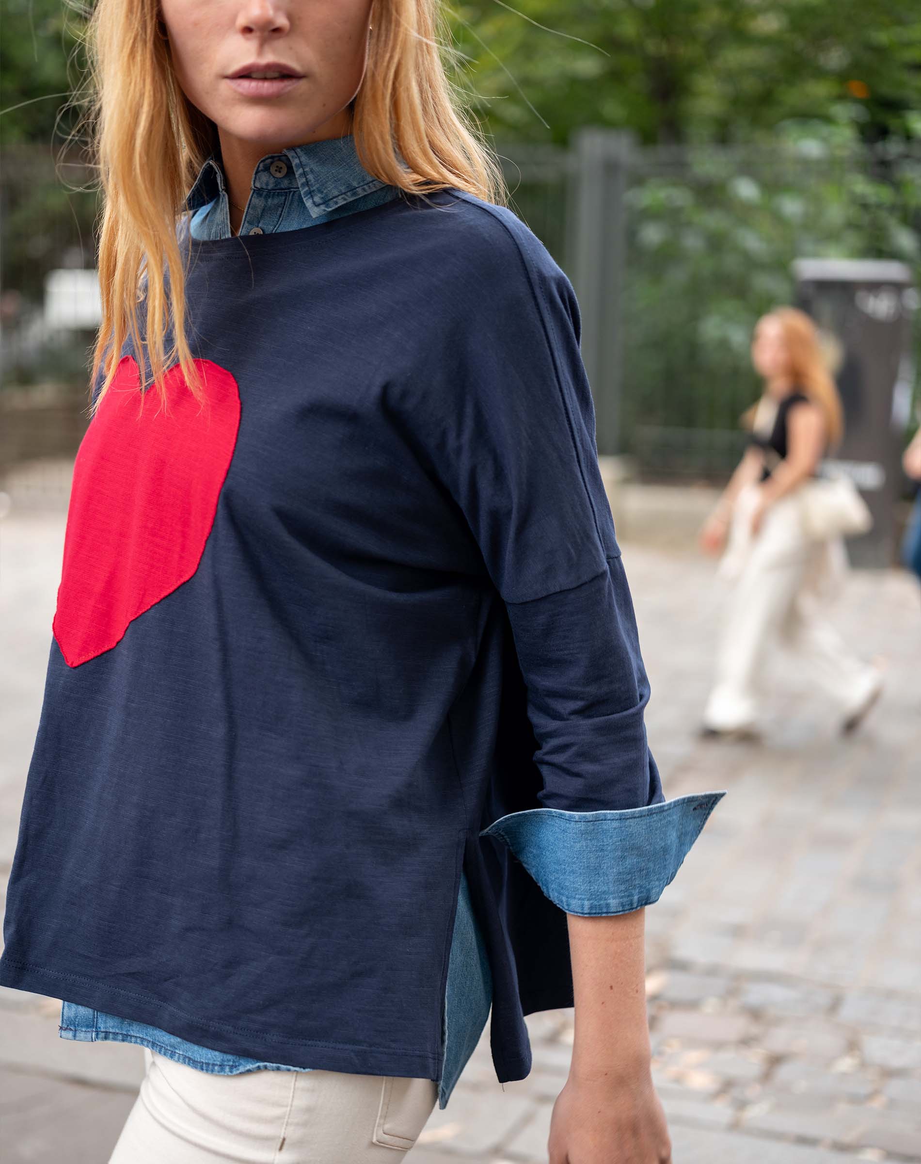 Person wearing a navy blue shirt with a red heart design and denim collar in an outdoor setting.