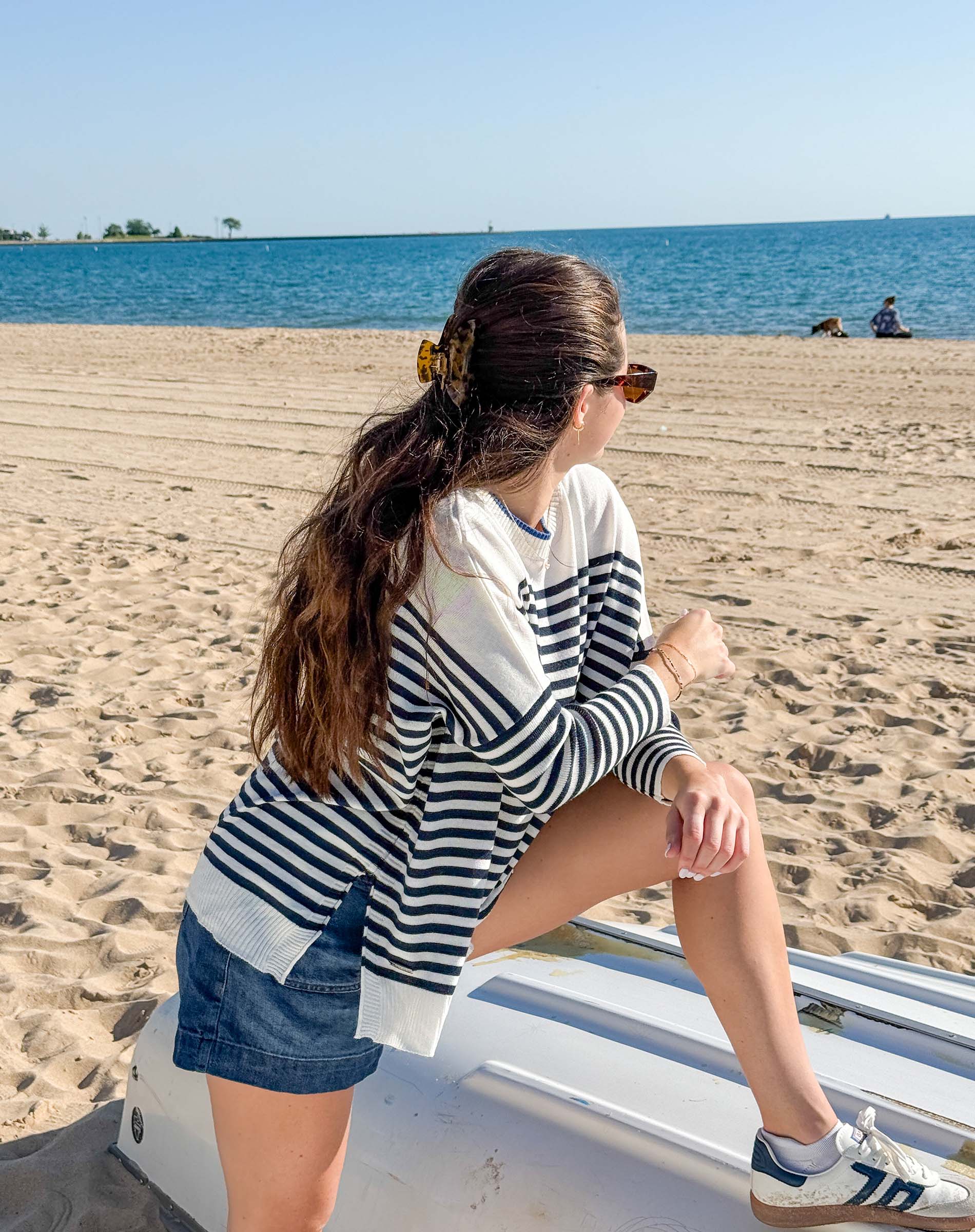 Woman sitting on a boat at the beach with a clear blue sky and water.