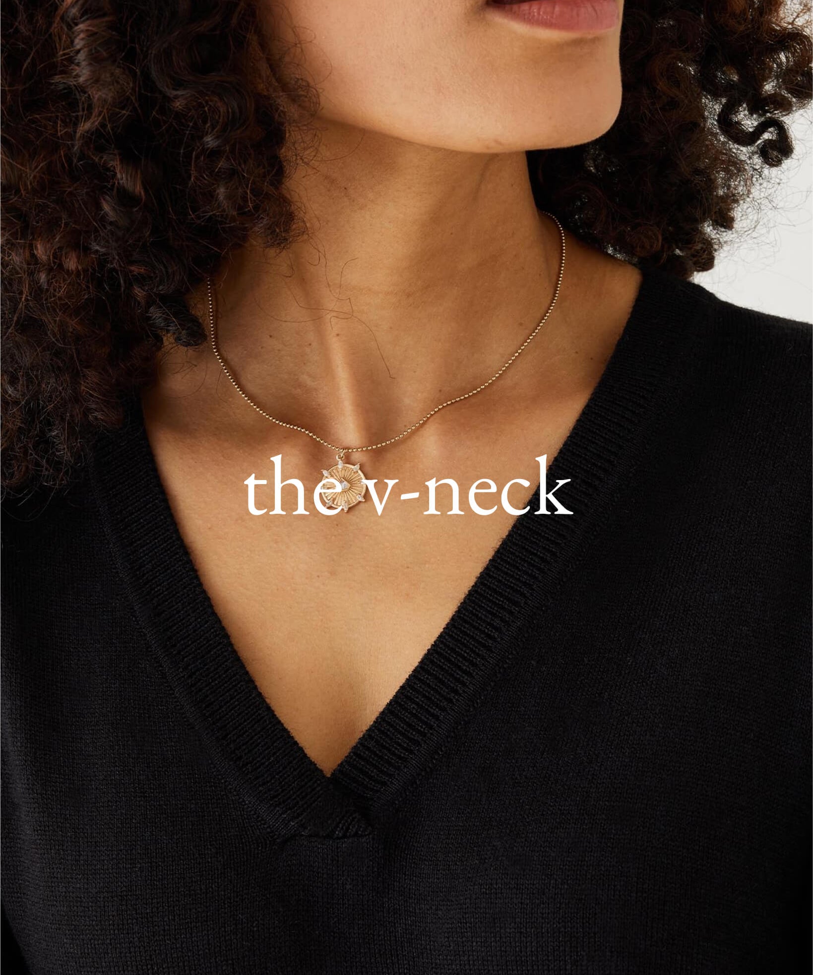Woman wearing a black V-neck sweater with a gold necklace, featuring the text 'the v-neck'.