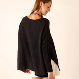 Woman wearing a black poncho against a beige background