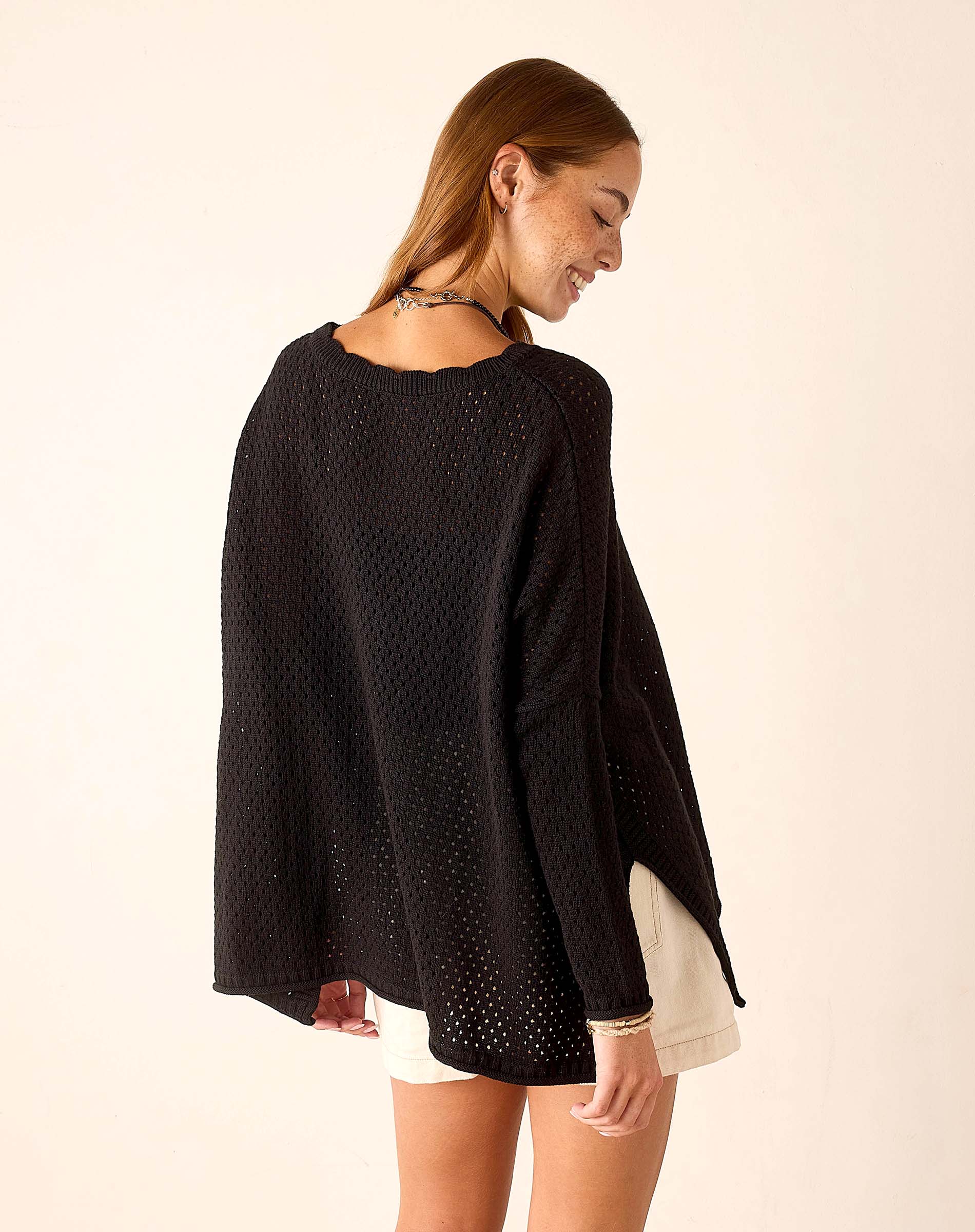 Woman wearing a black poncho against a beige background