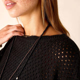 Close-up of a person wearing a black knit sweater with a beige background